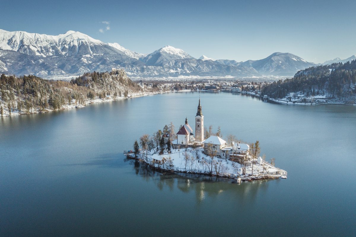 Panoramic view of famous Bled Island (Blejski otok) at scenic Lake Bled with Bled Castle (Blejski grad) and Julian Alps in the background on a beautiful sunny day in winter, Slovenia