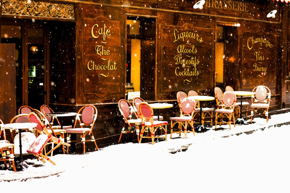 Wooden parisian coffee house with it's sidewalk tables and chairs in winter with the snow falling