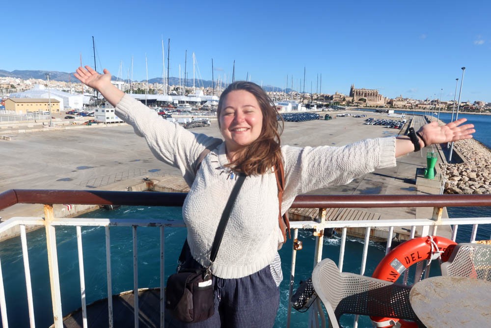 Girl standing on the deck of the Palma to Barcelona ferry with her arms in the air, looking happy