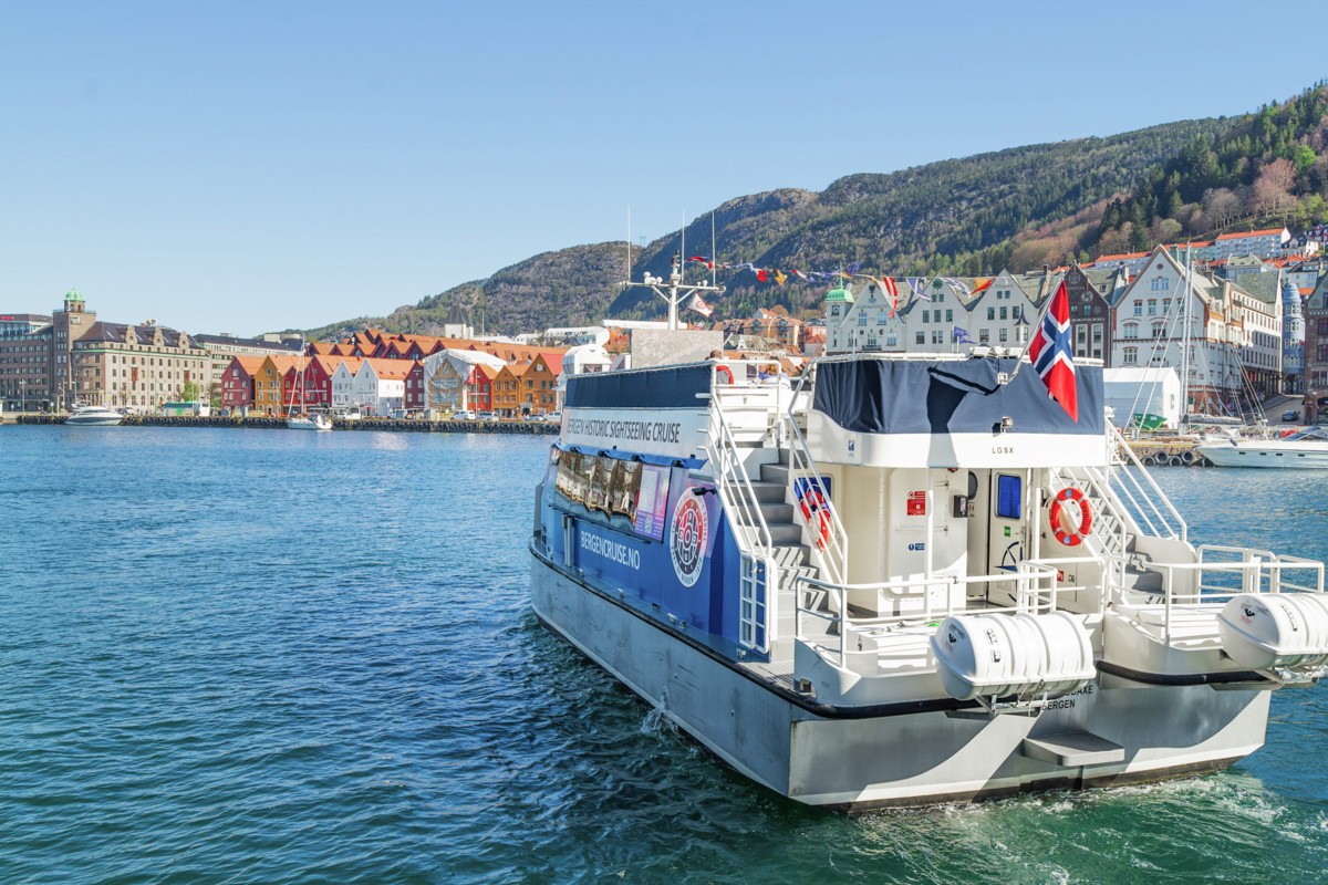 Sightseeing cruise boat leaving from Bergen, with yellow and red buildings and hills in the background