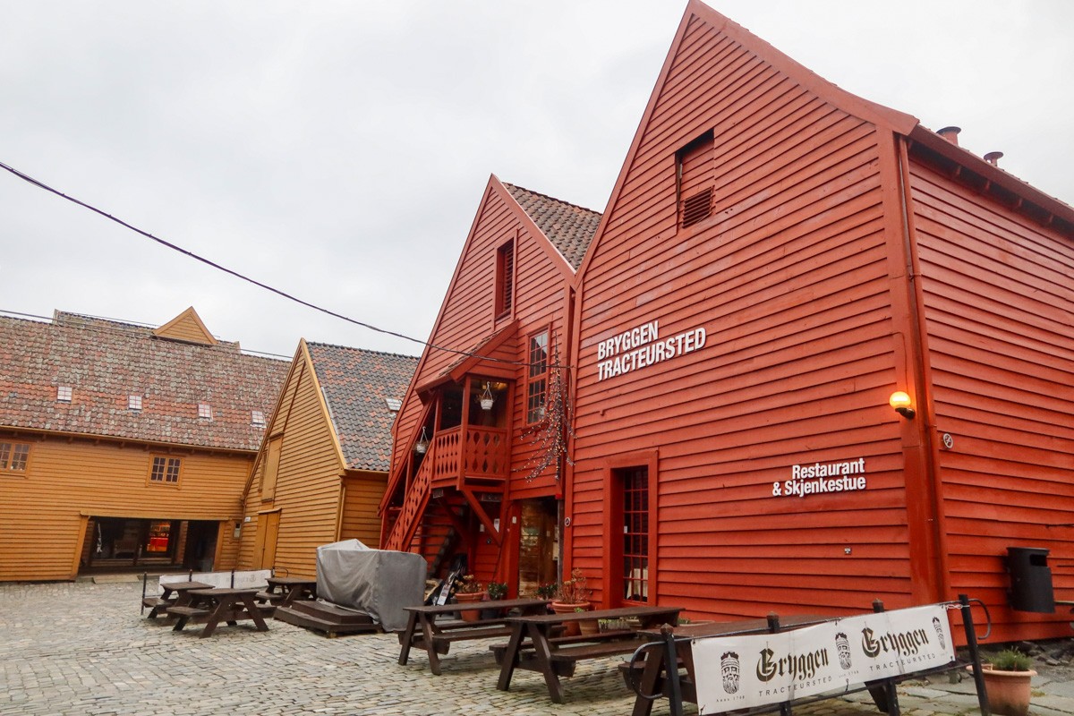 Red and yellow wooden buildings, housing a museum, in the heart of Bergen, with a cloudy sky in the background