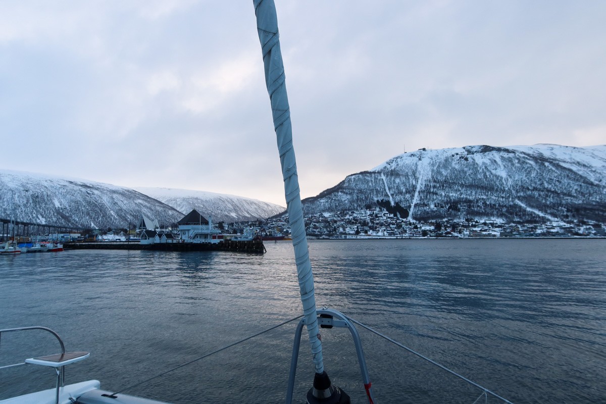 Embarking on a fjord tour in Tromso, with snowy mountains in background, the boat is sailing over the waters of the harbour