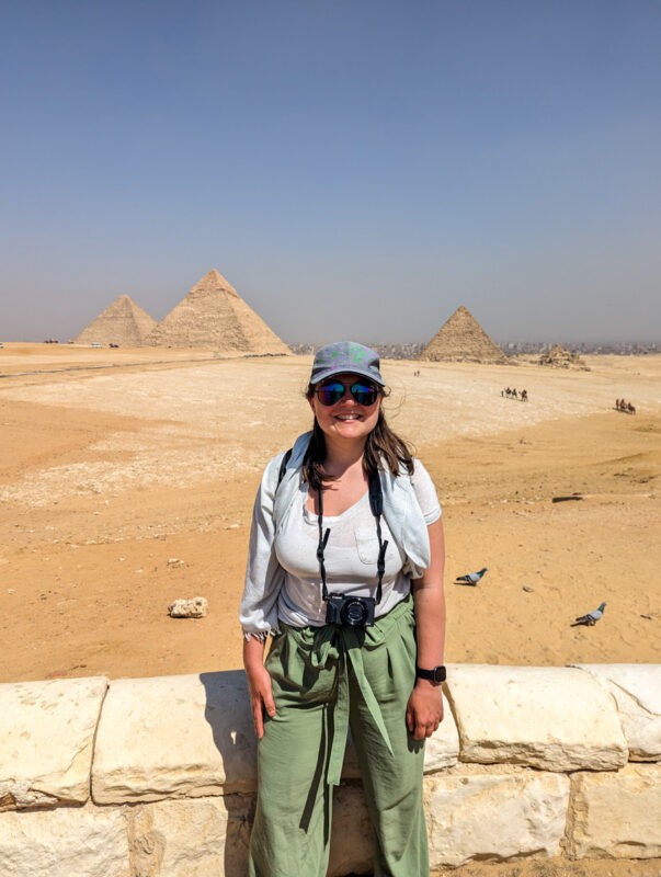 Claire standing in front of the pyramids of Giza which sit in the middle of a desert in Egypt