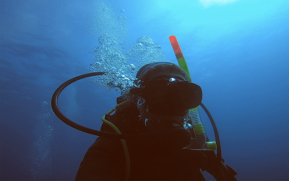 Claire underwater, with bubbles going up from her regulator, diving in Malta