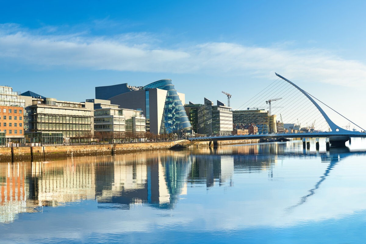 Modern buildings and offices on Liffey river in Dublin on a bright sunny day, bridge on the right is a famous Harp bridge.