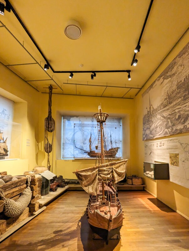 An exhibit displaying a scale model of a historic ship, surrounded by maritime artifacts, located within a museum in Tallinn