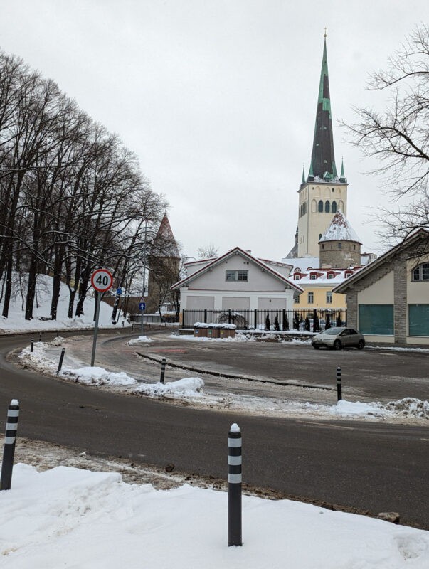 A snowy street view in Tallinn, with a prominent church spire reaching into the overcast sky, typical of the city's winter landscape.