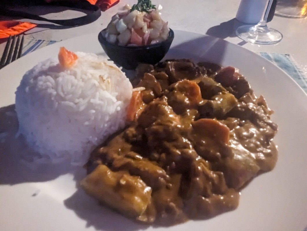 Plate of traditional Gambian peanut stew served with white rice and a side salad, captured in a dimly lit setting indicative of an evening meal.