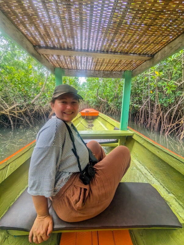 Smiling woman sitting on a boat covered with a thatched roof, prepared for a river tour through dense mangroves in The Gambia.