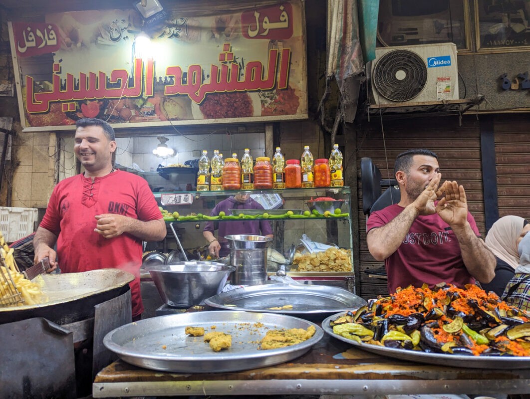 A vibrant street food stall in Cairo, with a cheerful vendor preparing dishes and a variety of colorful cooked vegetables on display.