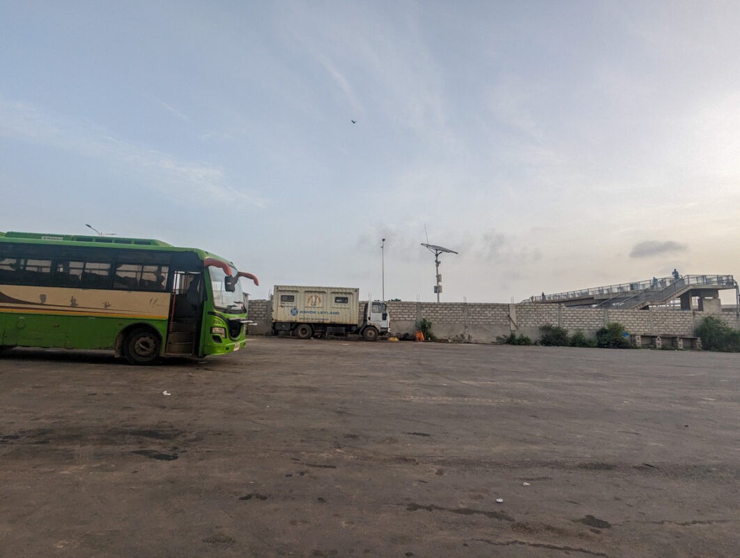 Sunrise at a spacious Senegalese transport hub with a green bus, ready to start its journey, under a pastel sky.