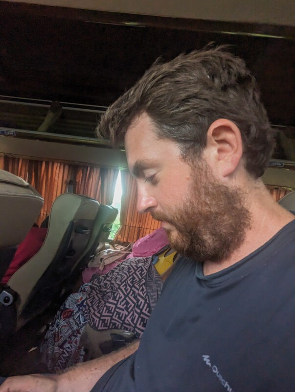 A candid shot of a man sitting on a bus, looking down thoughtfully.