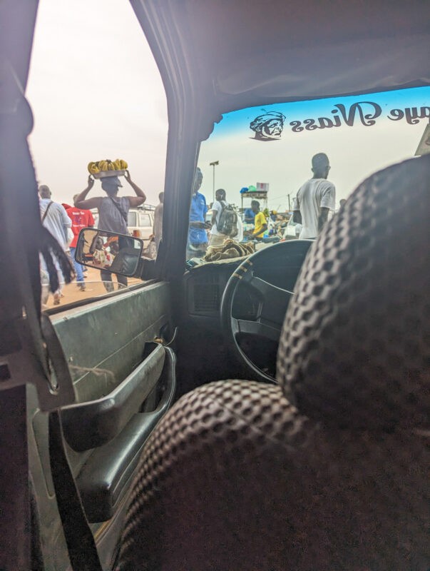 "View from the inside of a 'sept-places' showing a crowded market scene through the car window, highlighting the vibrant street life in Senegal.