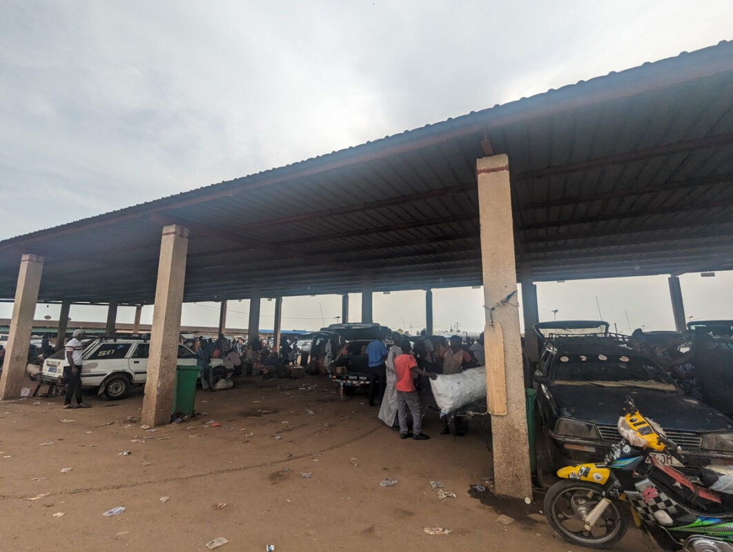 A covered market area with various 'sept-places' cars and people engaging in daily activities, depicting a typical day in Senegalese public transport spots