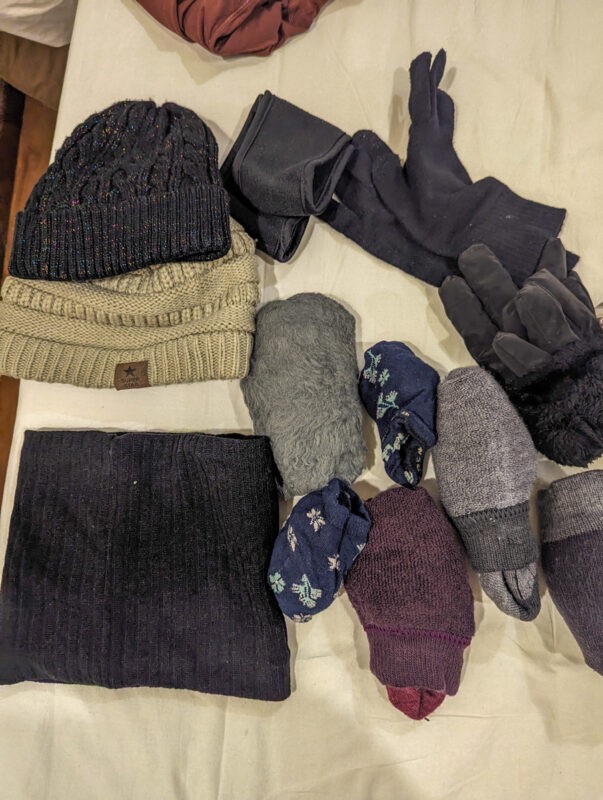 A collection of winter accessories such as black and beige knit hats, gloves, various socks in different colors and patterns, and a black scarf.