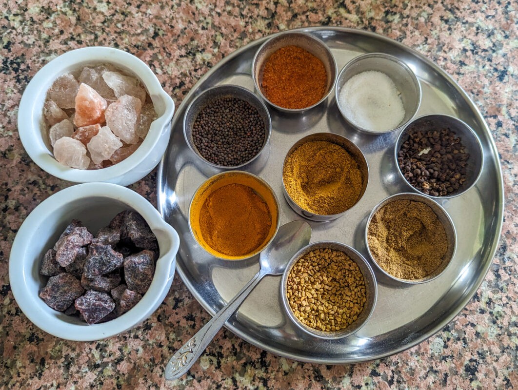 A stainless steel tray divided into compartments filled with various spices and seasonings, including whole and ground forms.