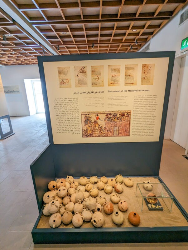 A museum display with text titled "The assault of the Medieval fortresses" accompanied by artifacts, including a collection of ancient pottery.