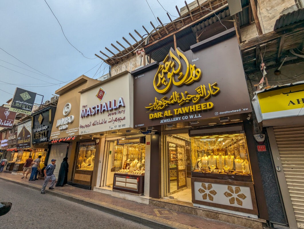A street view of jewelry stores, including "Mashalla Jewellery" and "Dar Al Tawheed Jewellery Co W.L.L," with people walking by