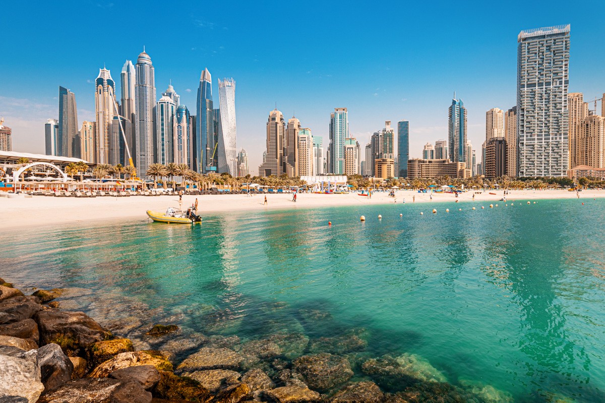 Luxurious and spectacular sandy beach with vacationers in the Dubai Marina and JBR area with tall skyscrapers and hotels in the background